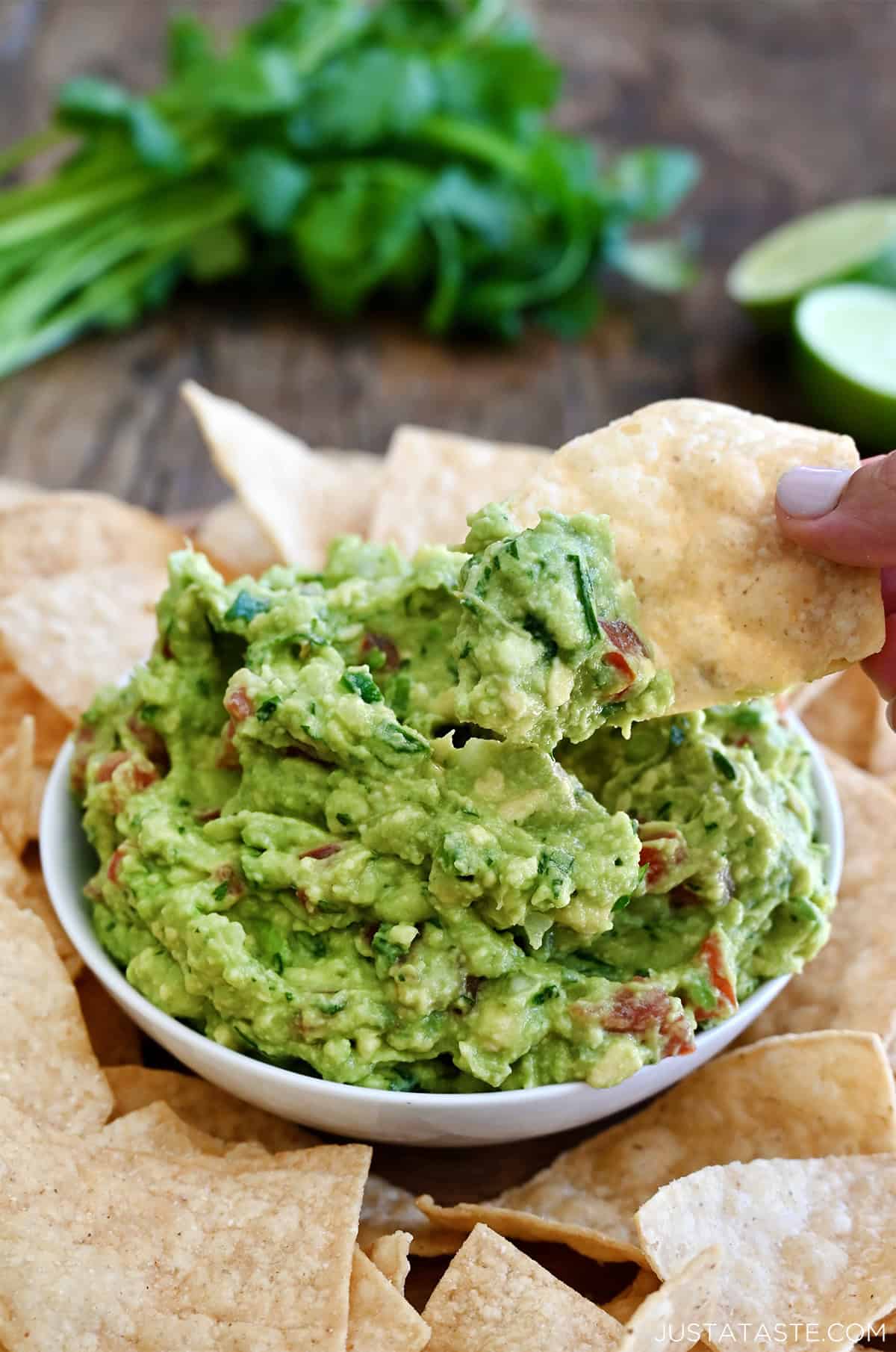 Homemade guacamole in a bowl on a serving plate surrounded by tortilla chips.