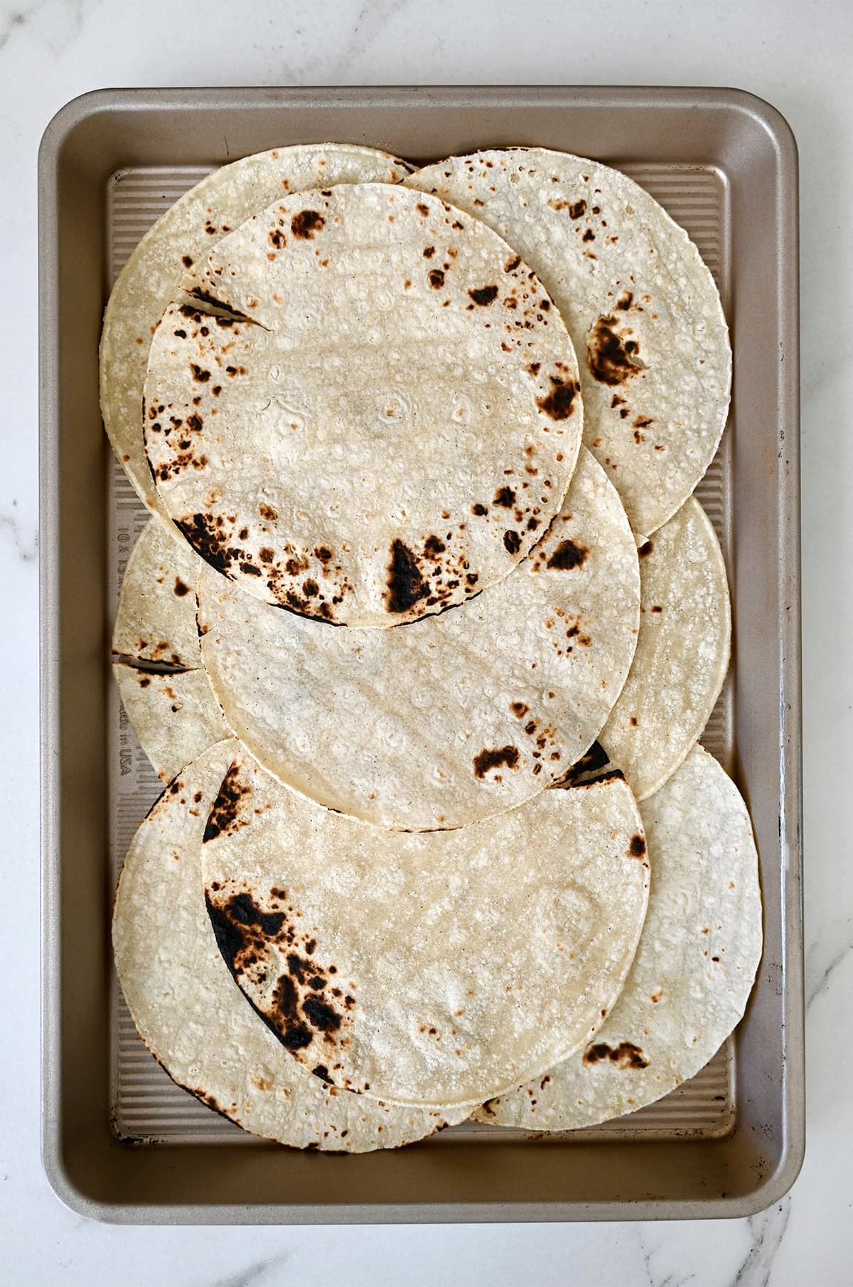 Blistered corn tortillas on a baking sheet.