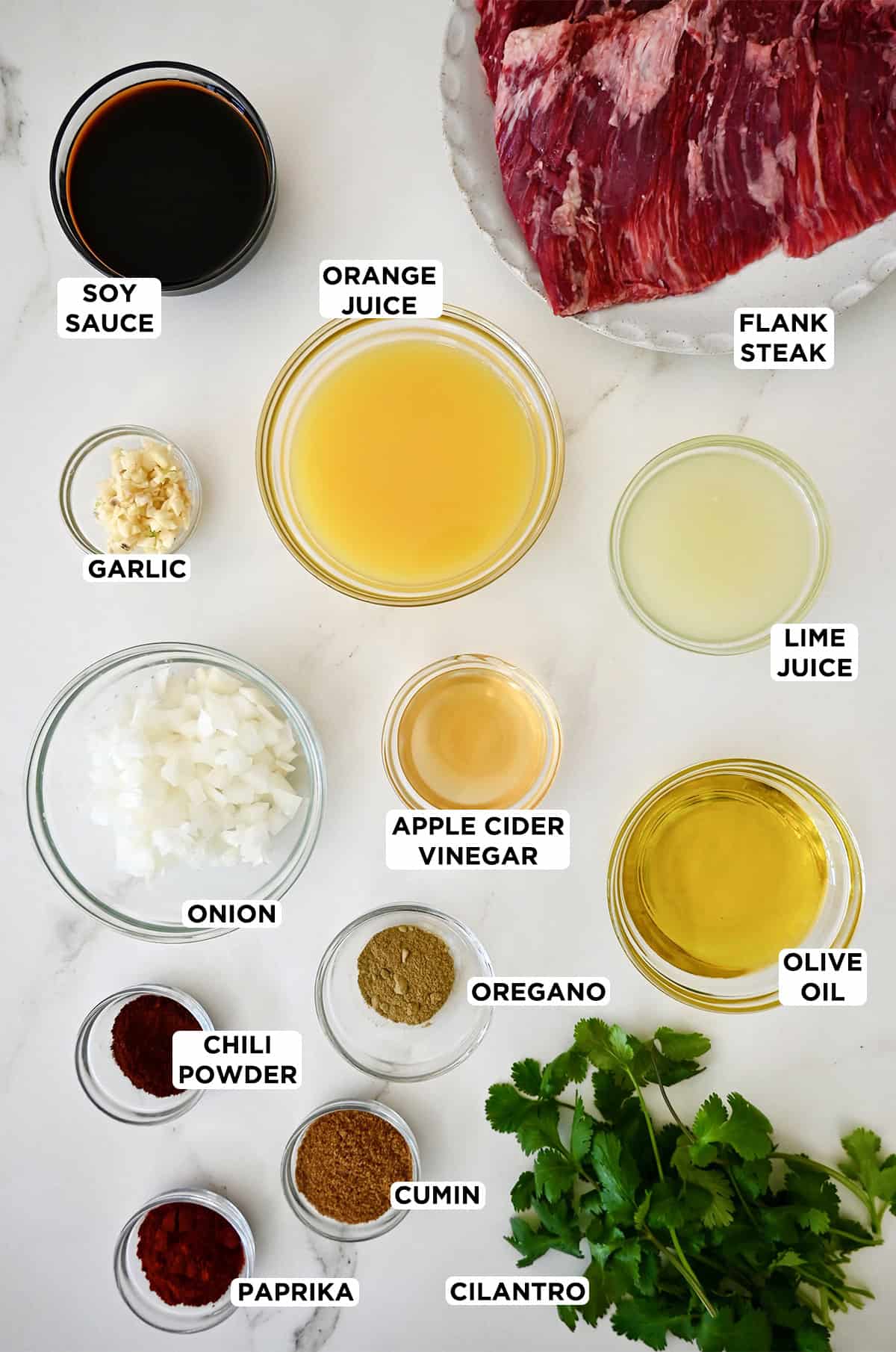 Ingredients to make a marinade for carne asada next to flank steak on a plate.