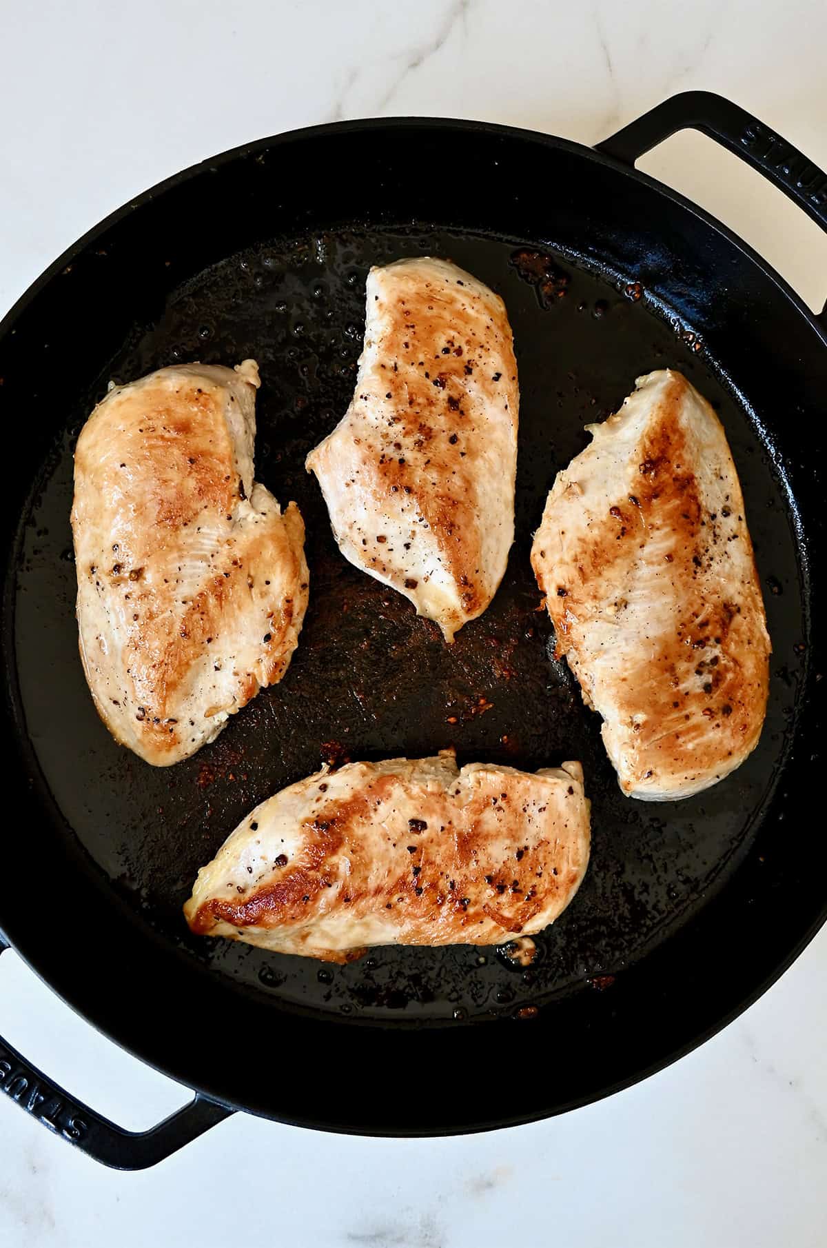 Four boneless, skinless chicken breasts in a large skillet.