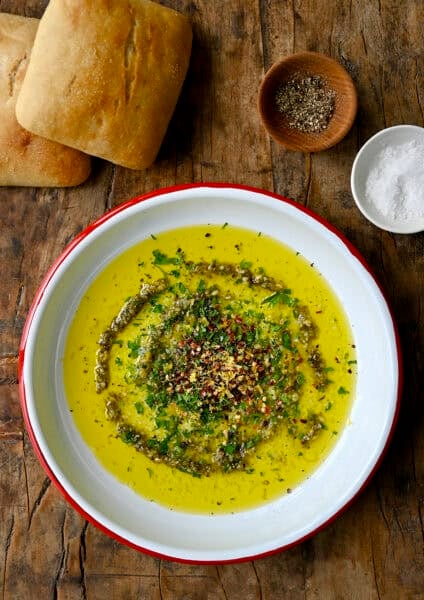 Italian bread dipping oil on a plate with two ciabatta rolls nearby.