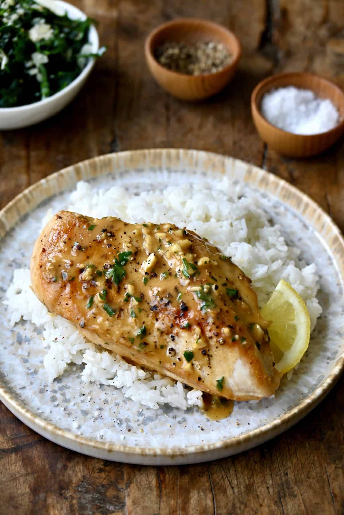 Garlic butter chicken breasts atop steamed white rice on a dinner plate.