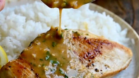 Spooning homemade garlic butter sauce over a juicy chicken breast on a plate with white rice.