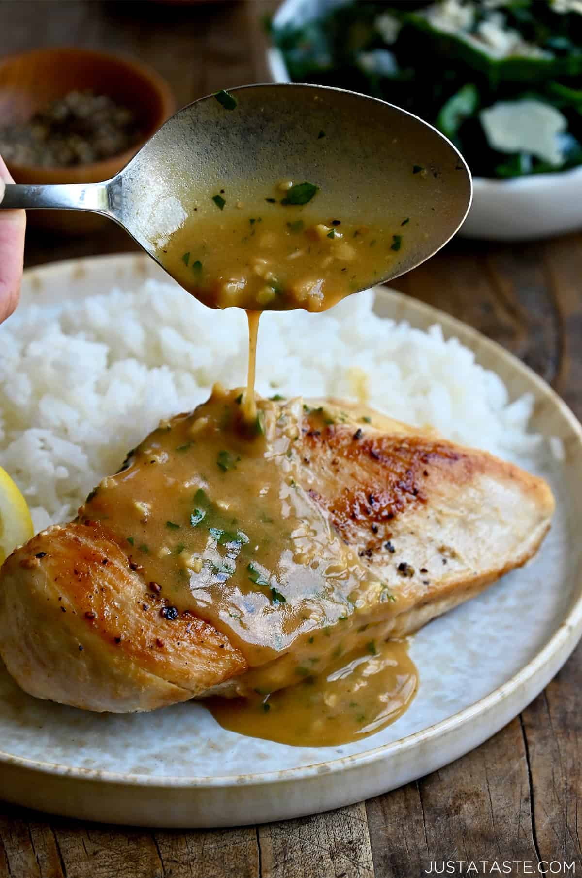 Spooning homemade garlic butter sauce over a juicy chicken breast on a plate with white rice.