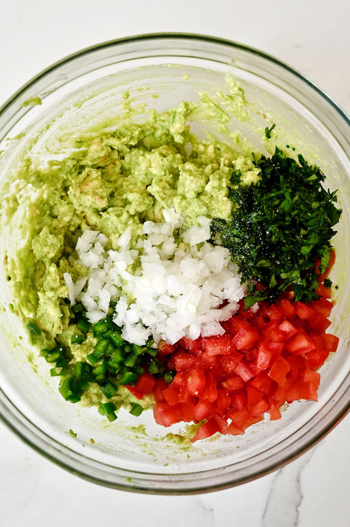All the ingredients to make guacamole in a glass prep bowl before mixing.