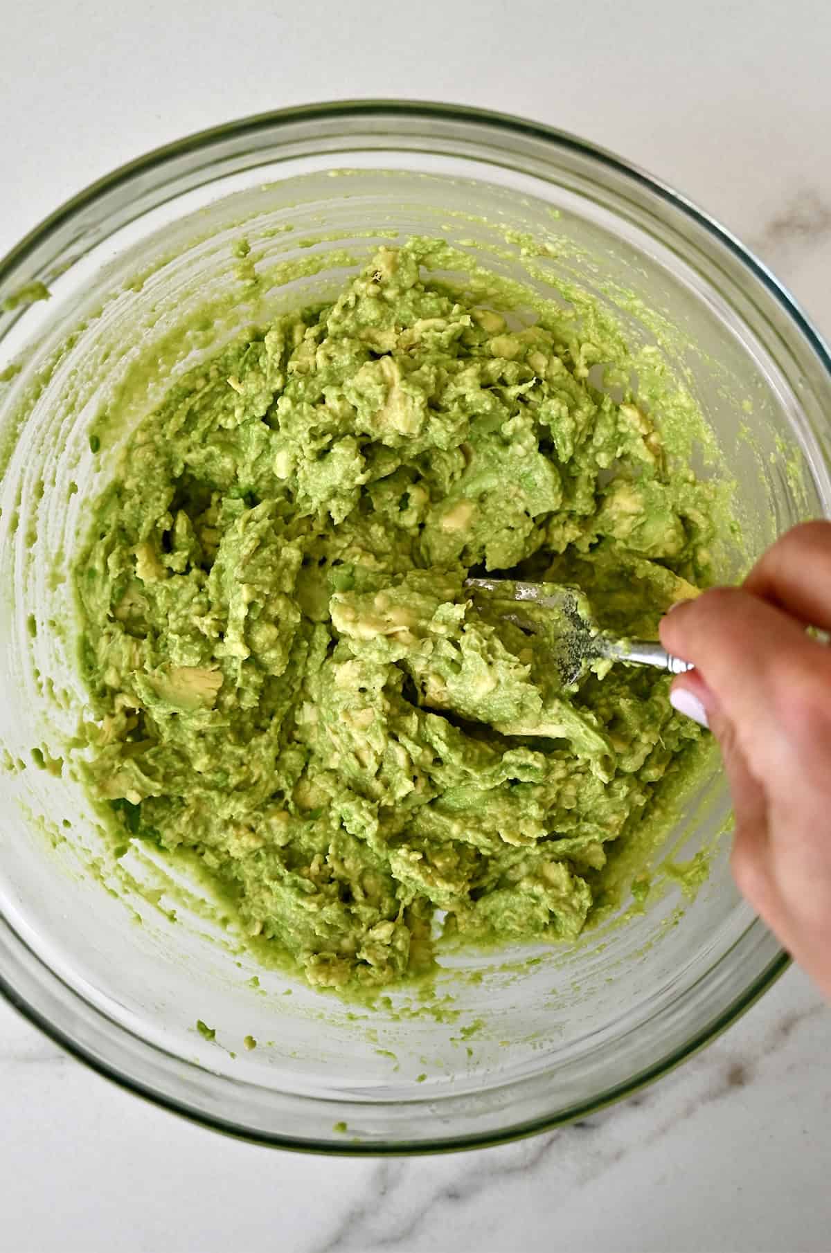 Mashing ripe avocado in a bowl with a fork.