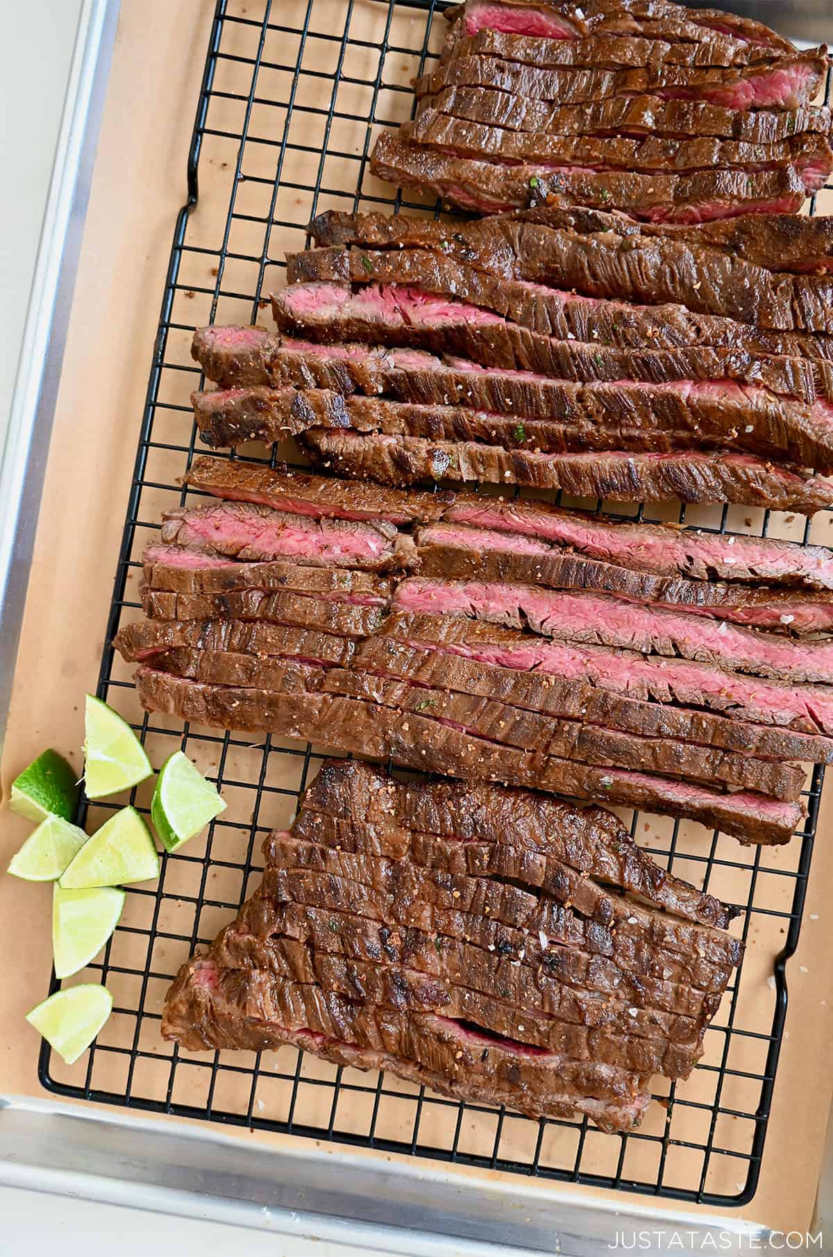 Thinly sliced carne asada on a cutting board with lime wedges.