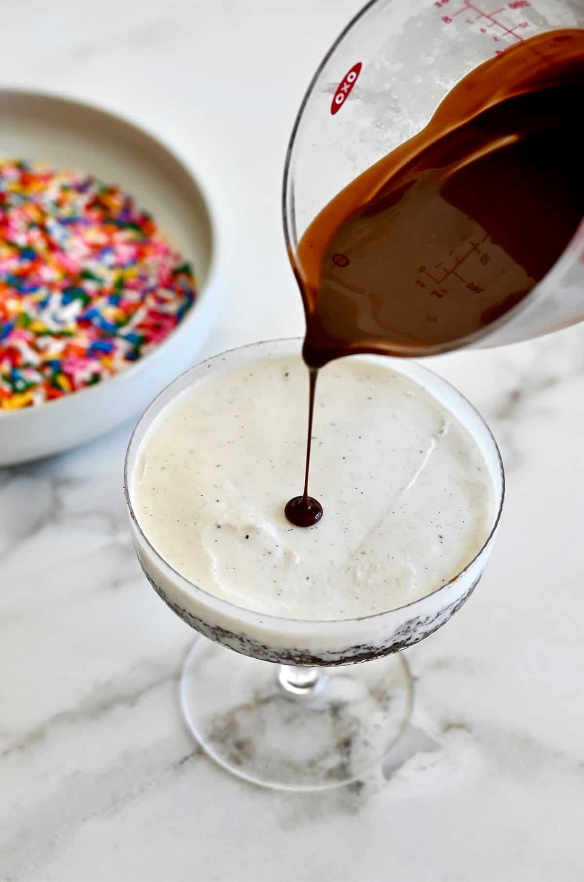 Pouring Magic Shell on top of a smooth layer of ice cream in a cocktail glass with cake.