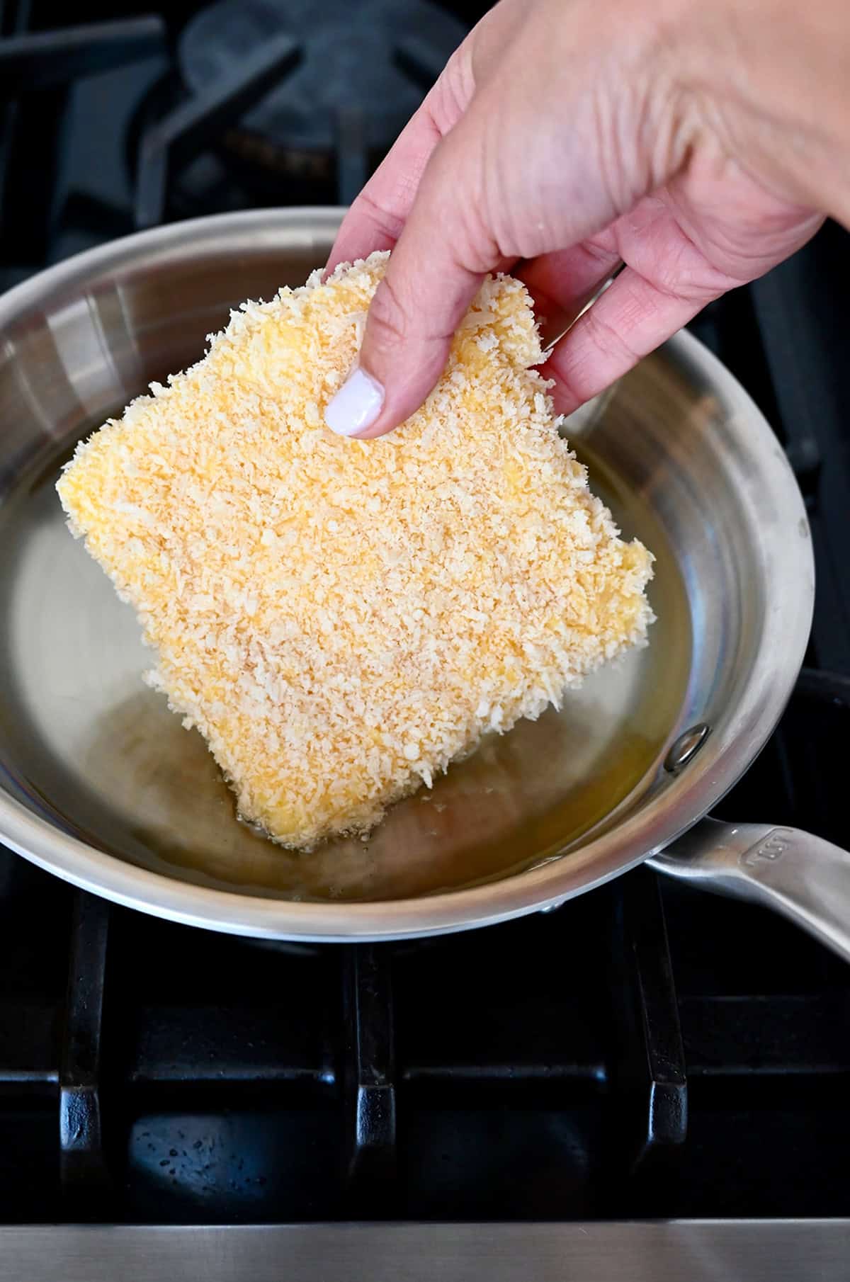Adding breaded mozzarella to a pan with a shallow layer of hot oil.