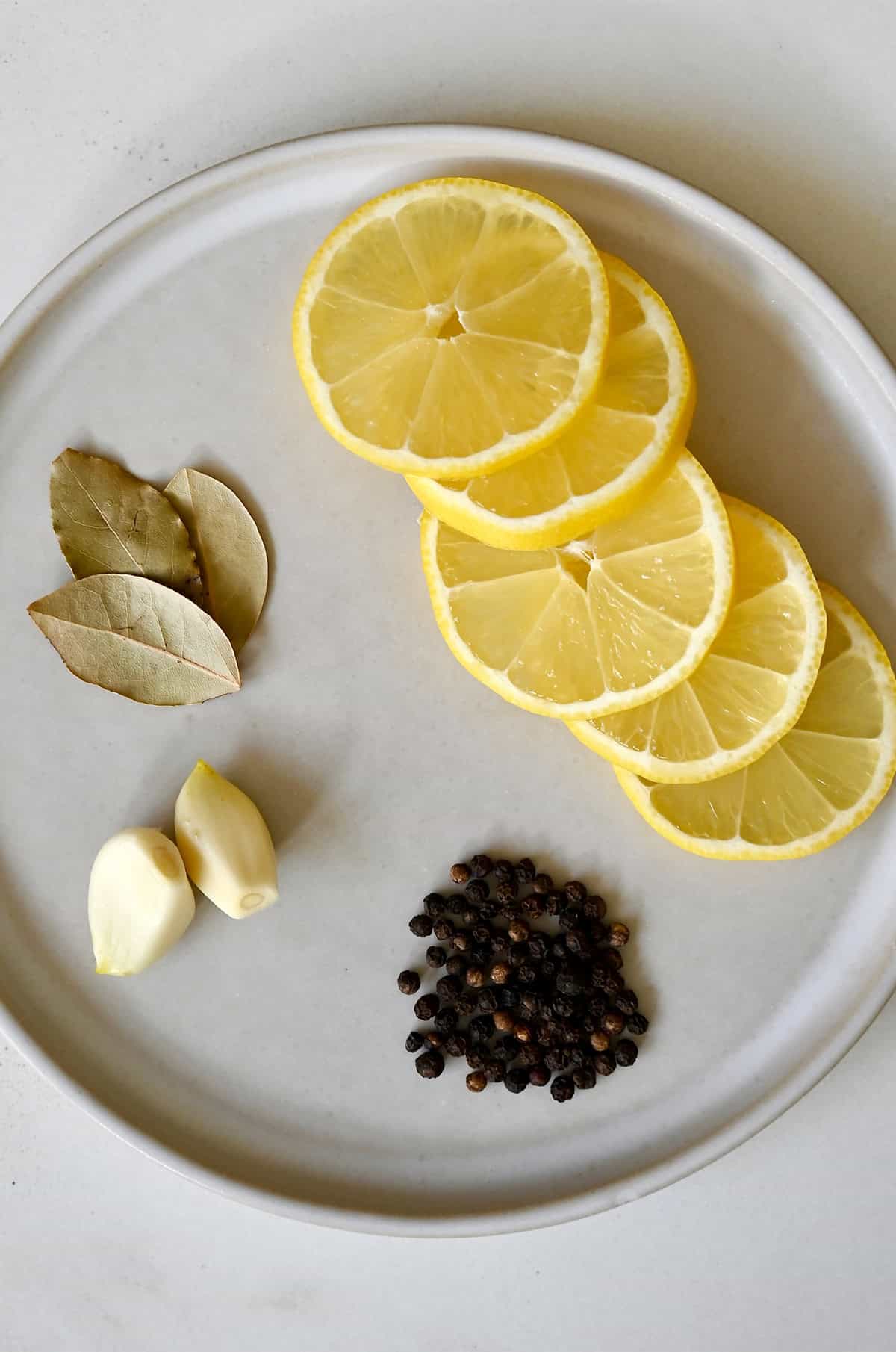 Aromatics for poaching chicken, including lemon slices, peppercorns, garlic cloves and bay leaves.
