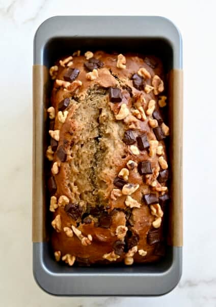 Golden brown cottage cheese banana bread with chocolate chips and chopped walnuts in a bread pan.