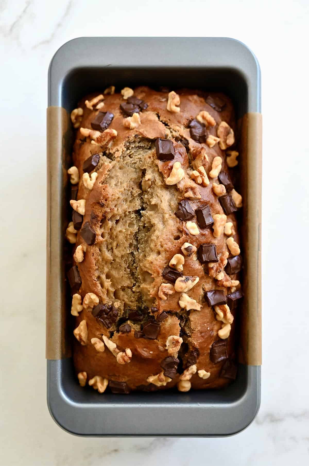 Golden brown cottage cheese banana bread with chocolate chips and chopped walnuts in a bread pan.
