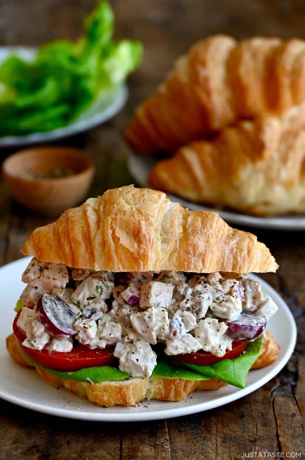 The best chicken salad recipe with grapes and walnuts on a buttery croissant with butter lettuce and a tomato slice.