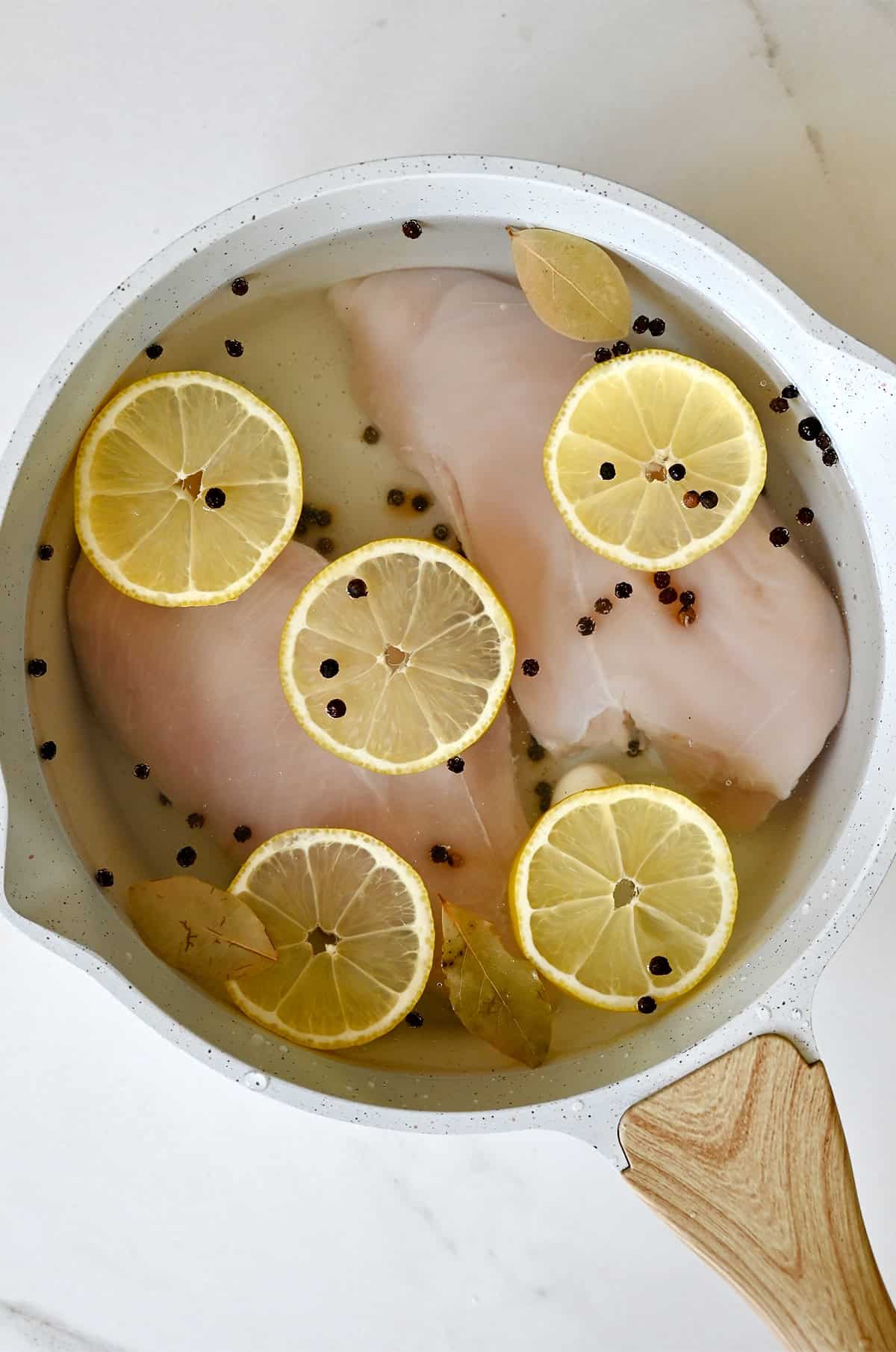 Chicken breasts are submerged in water with aromatics to poach.