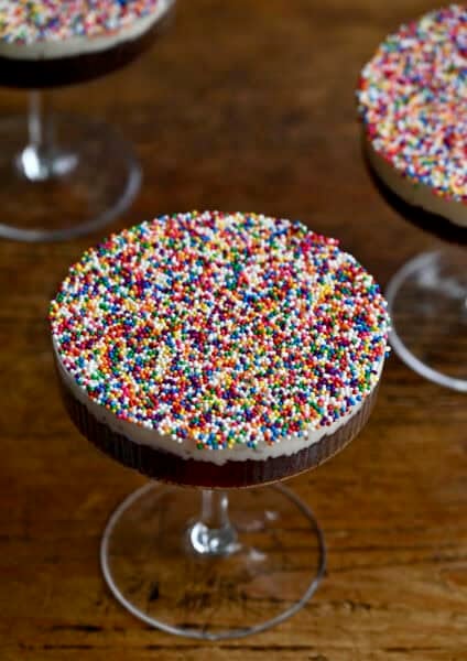 Cocktail dot cakes starring chocolate cake topped with vanilla buttercream frosting and a layer of rainbow sprinkles in a cocktail glass.