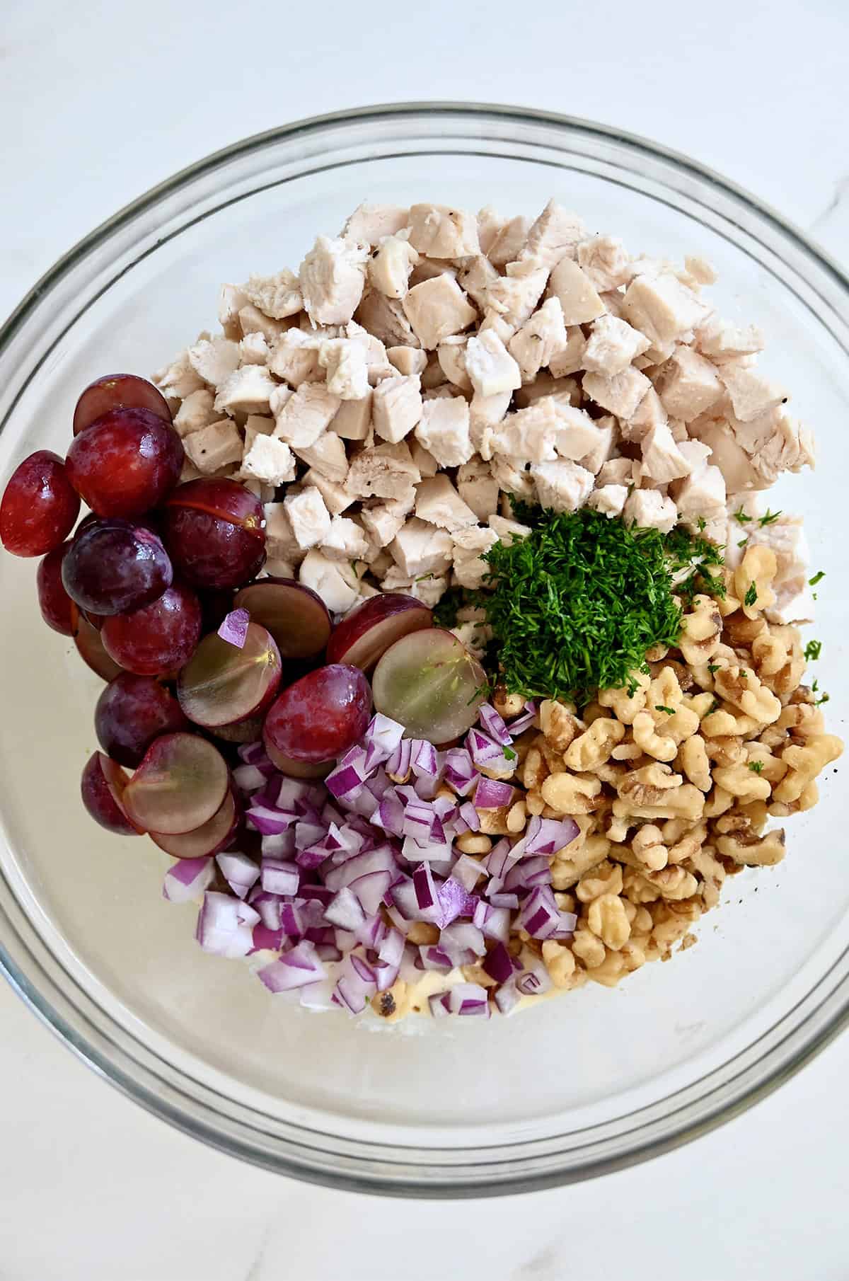 Chopped cooked chicken, halved red grapes, diced red onion, chopped fresh dill and chopped walnuts in a large mixing bowl.