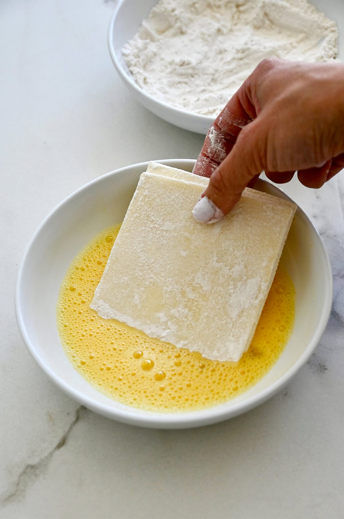 Dipping a stack of mozzarella slices into whisked egg.