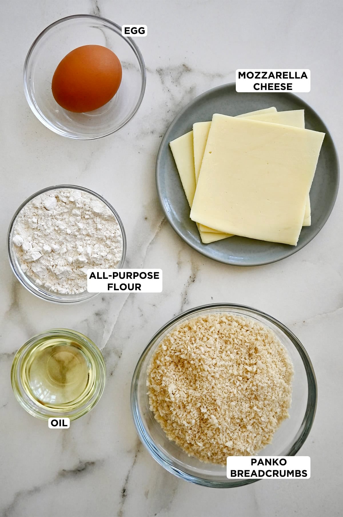 Ingredients to make pan-fried mozzarella, including slices of cheese, flour, Panko breadcrumbs, egg and oil.