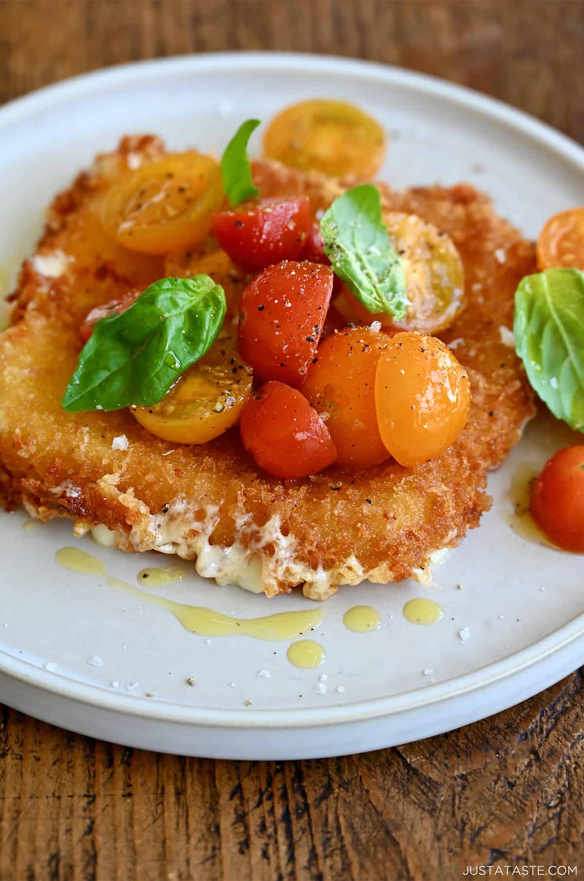Fried mozzarella topped with colorful cherry tomatoes and fresh basil leaves.