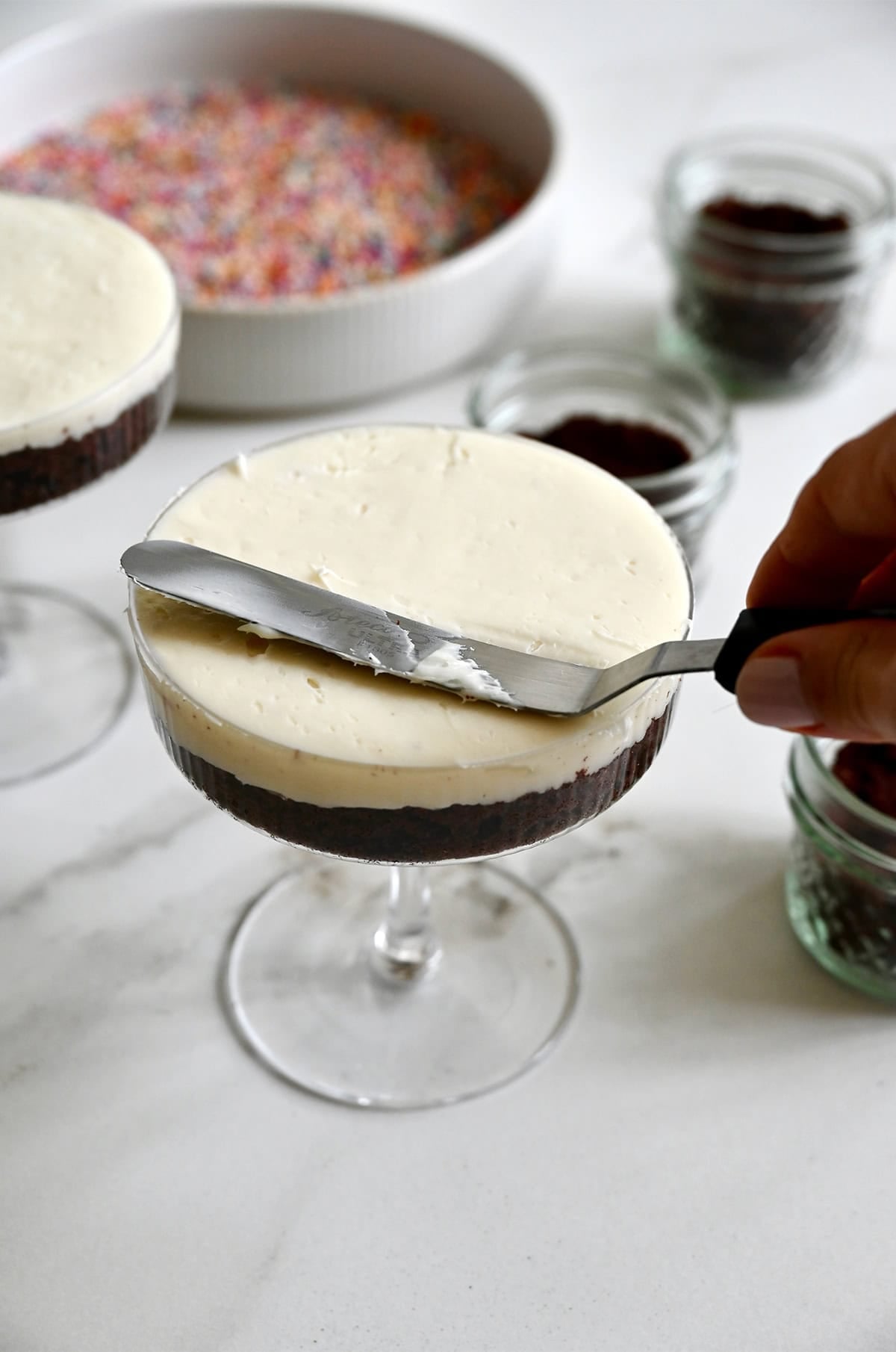 Using an offset spatula to frost an individual cake in a cocktail glass.