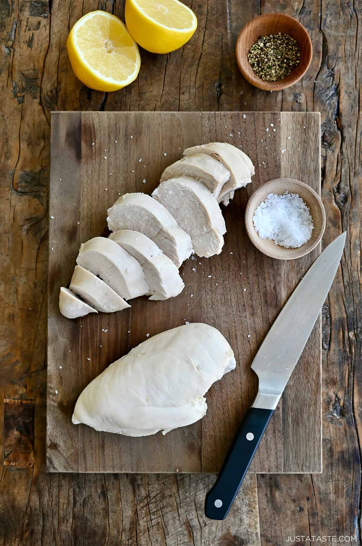 Poached chicken breasts on a cutting board with a chef's knife.