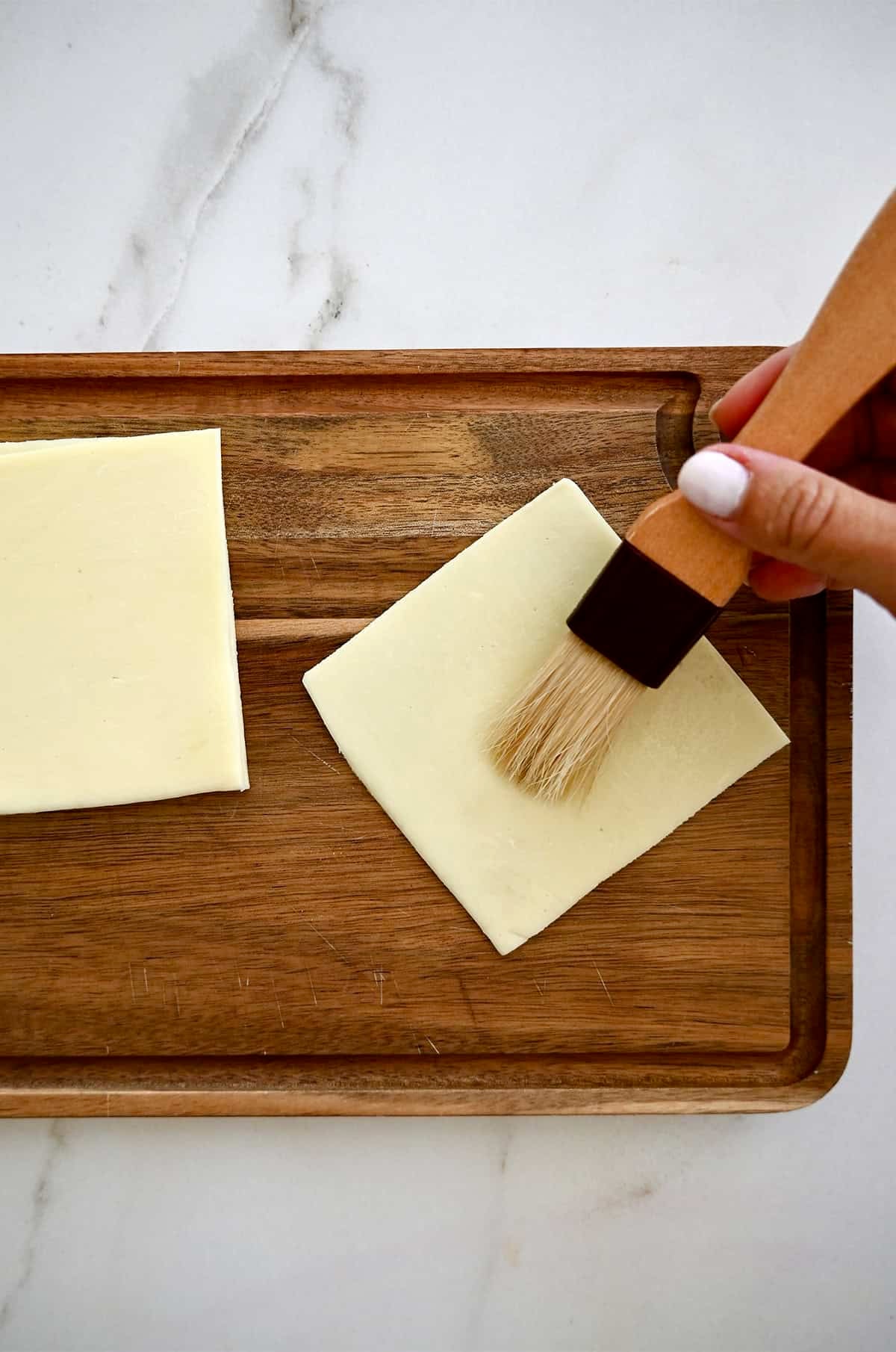 Brushing water onto a thin slice of mozzarella to seal it together with more slices.