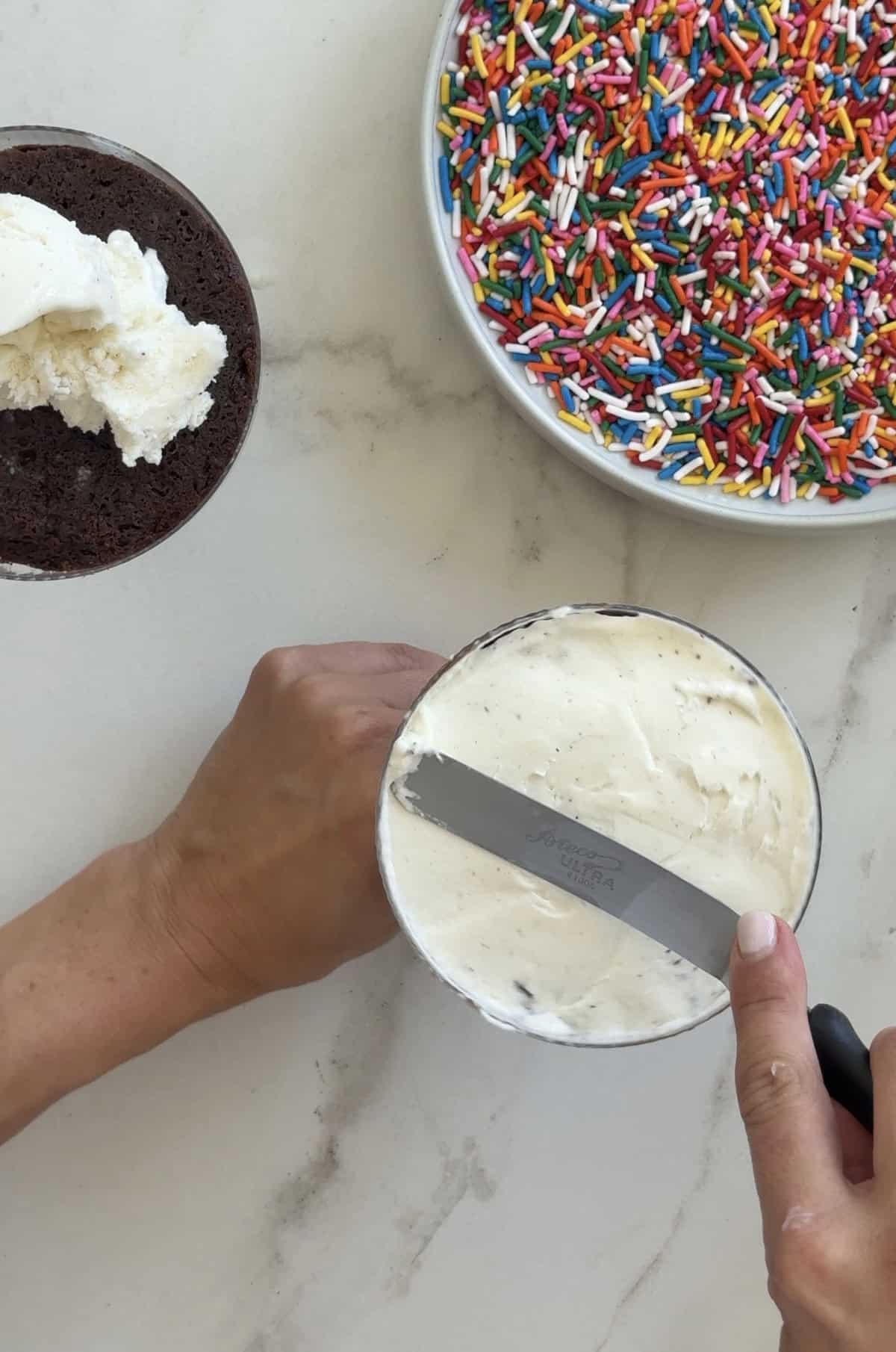 Slathering softened ice cream atop chocolate cake in a cocktail glass.