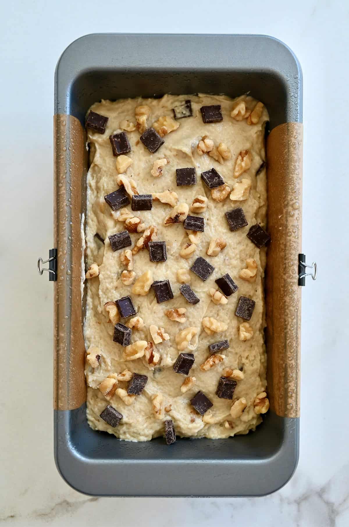 Unbaked cottage cheese banana bread topped with chocolate chunks and chopped walnuts in a parchment paper-lined loaf pan.