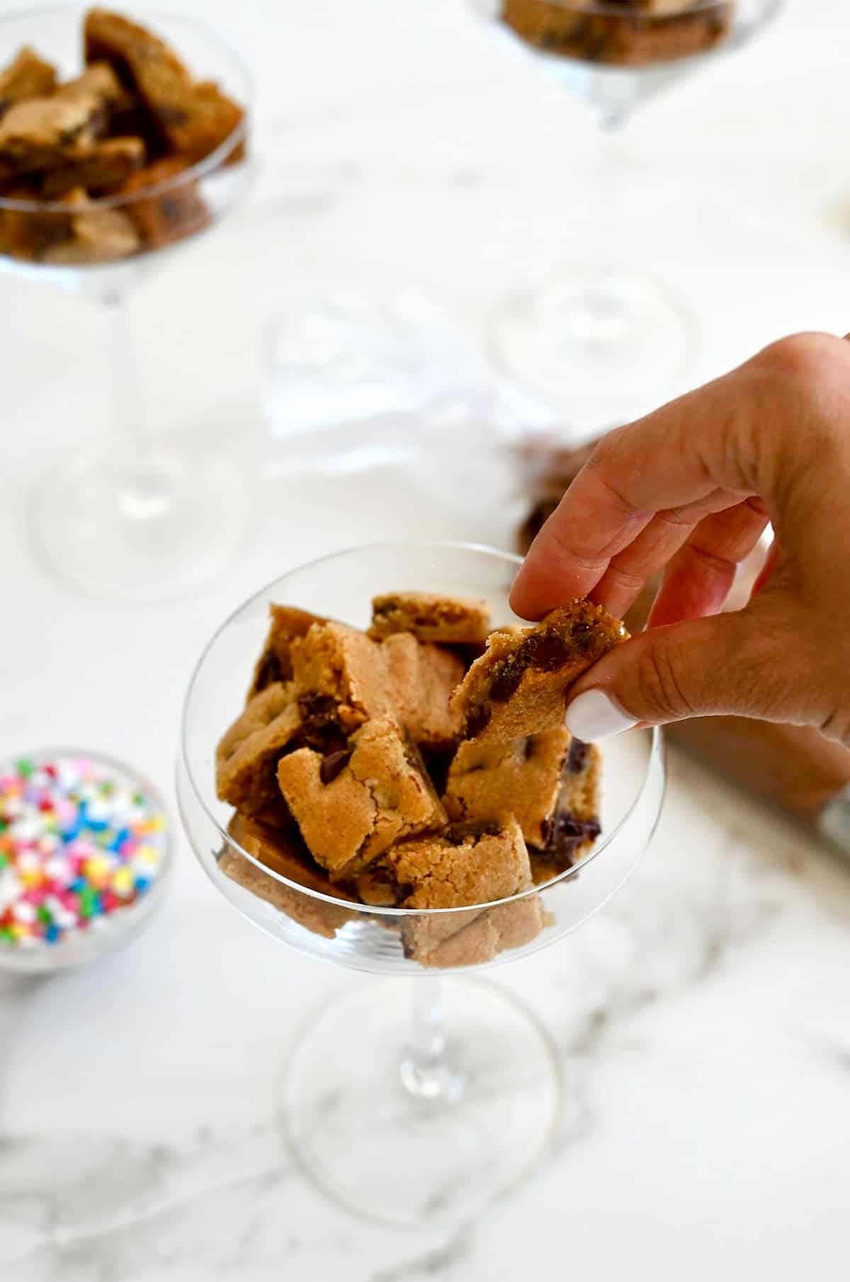 Adding cookie cake cubes to a martini glass.