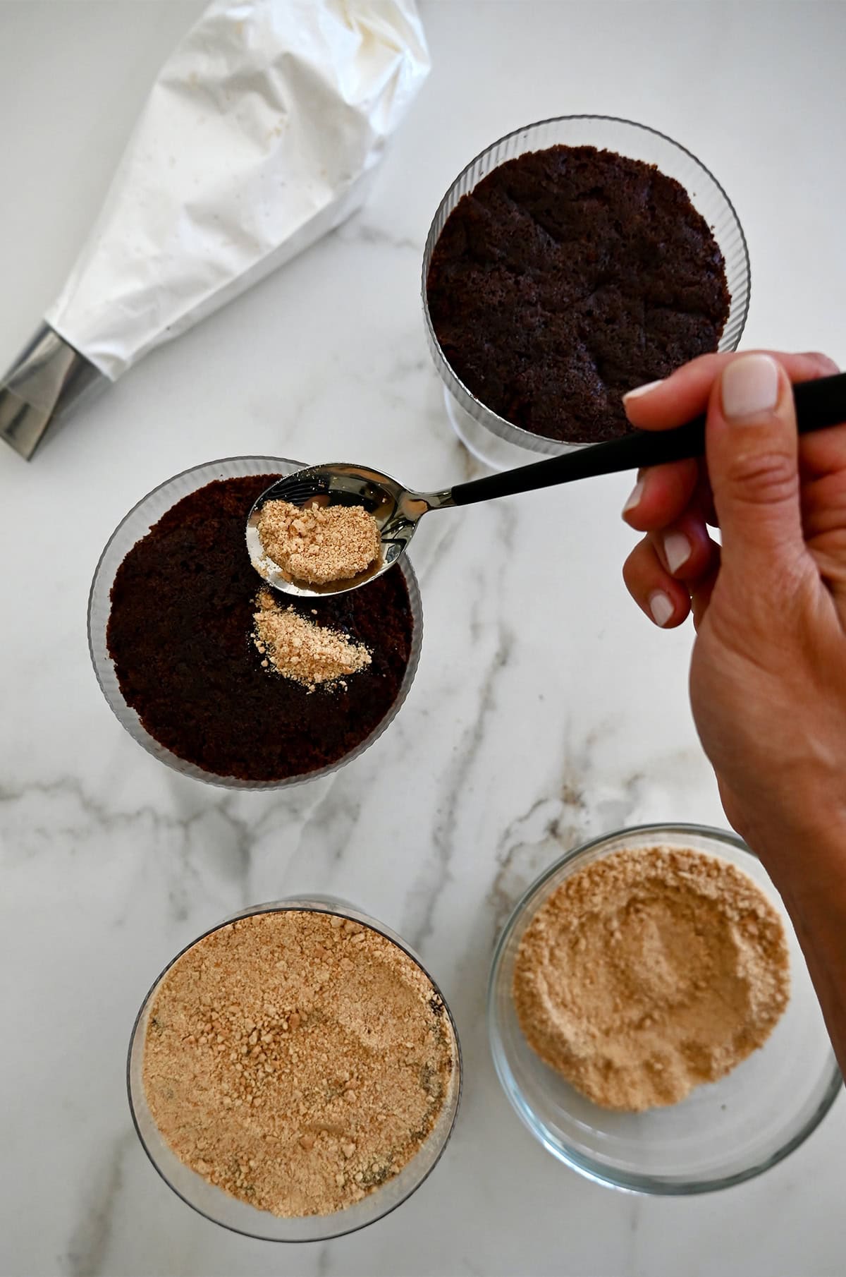 Adding graham cracker crumbs atop chocolate cake in a cocktail glass.