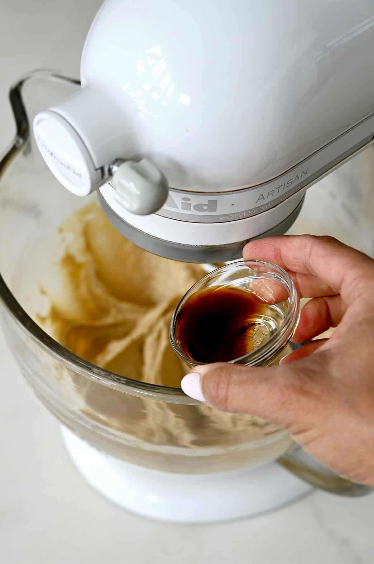 Adding vanilla extract to a stand mixer with creamed butter and sugar.