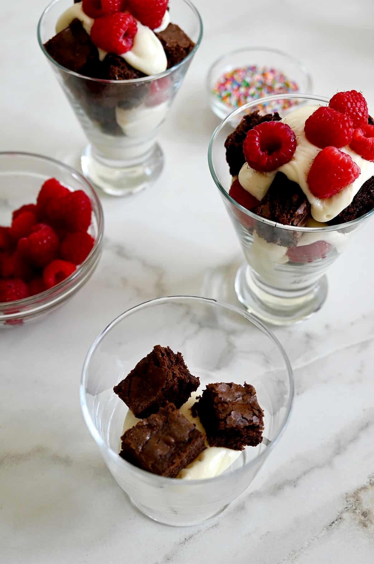 Layering brownie croutons, vanilla buttercream frosting and fresh raspberries into serving glasses.