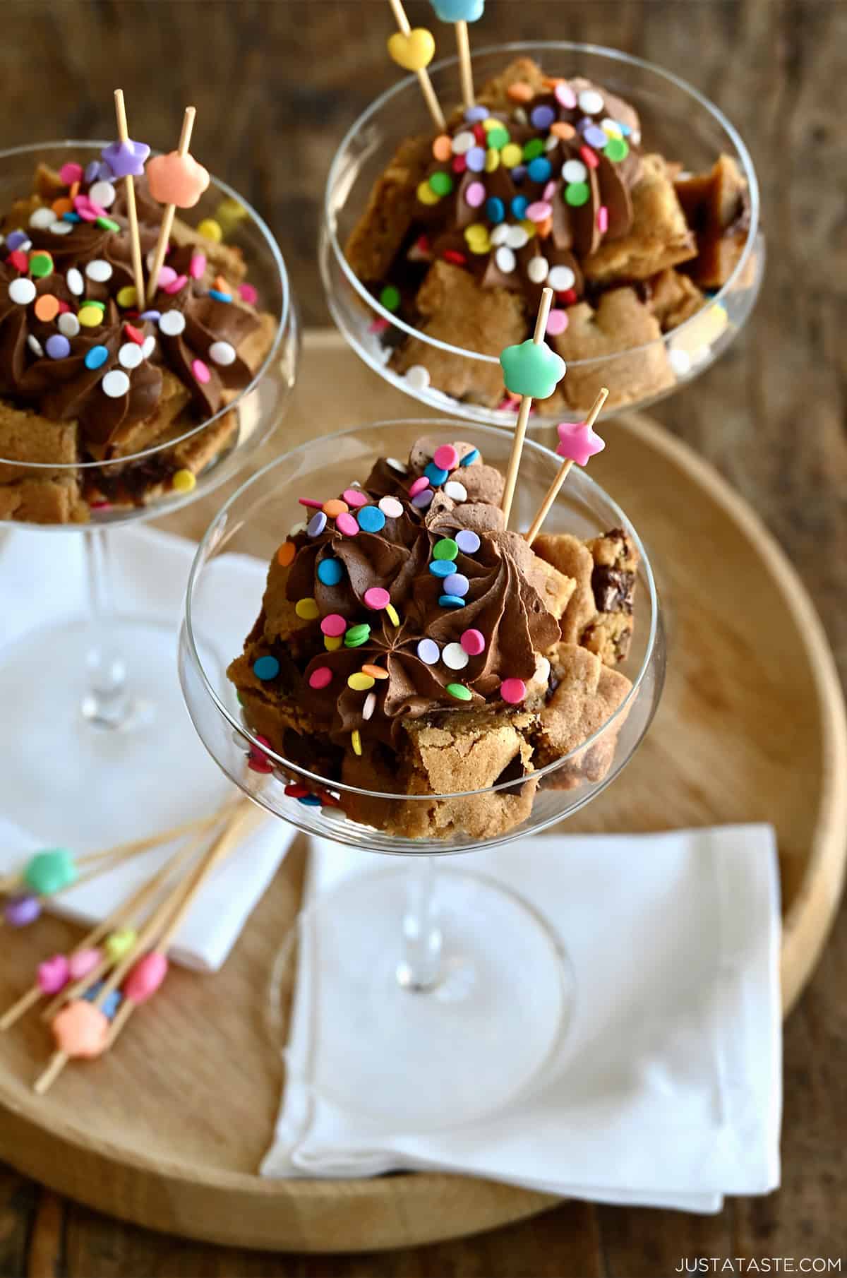 Cookie cocktail cakes served in martini glasses featuring layers of chocolate chip cookie cake, chocolate buttercream frosting and rainbow sprinkles.