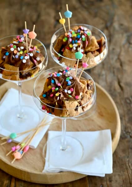 Chocolate chip cookie cake cut into cubes and layered in a cocktail glass with chocolate buttercream frosting and sprinkles.
