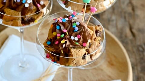 Chocolate chip cookie cake cut into cubes and layered in a cocktail glass with chocolate buttercream frosting and sprinkles.