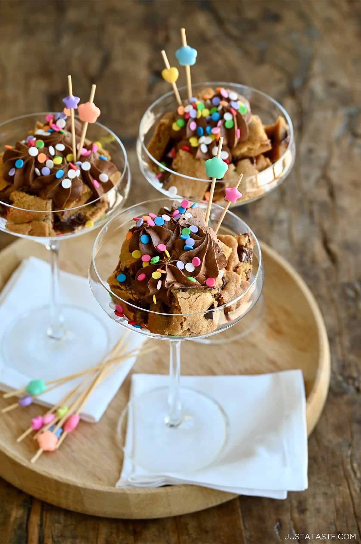 Chocolate chip cookie cake cut into cubes and layered in a cocktail glass with chocolate buttercream frosting and sprinkles.
