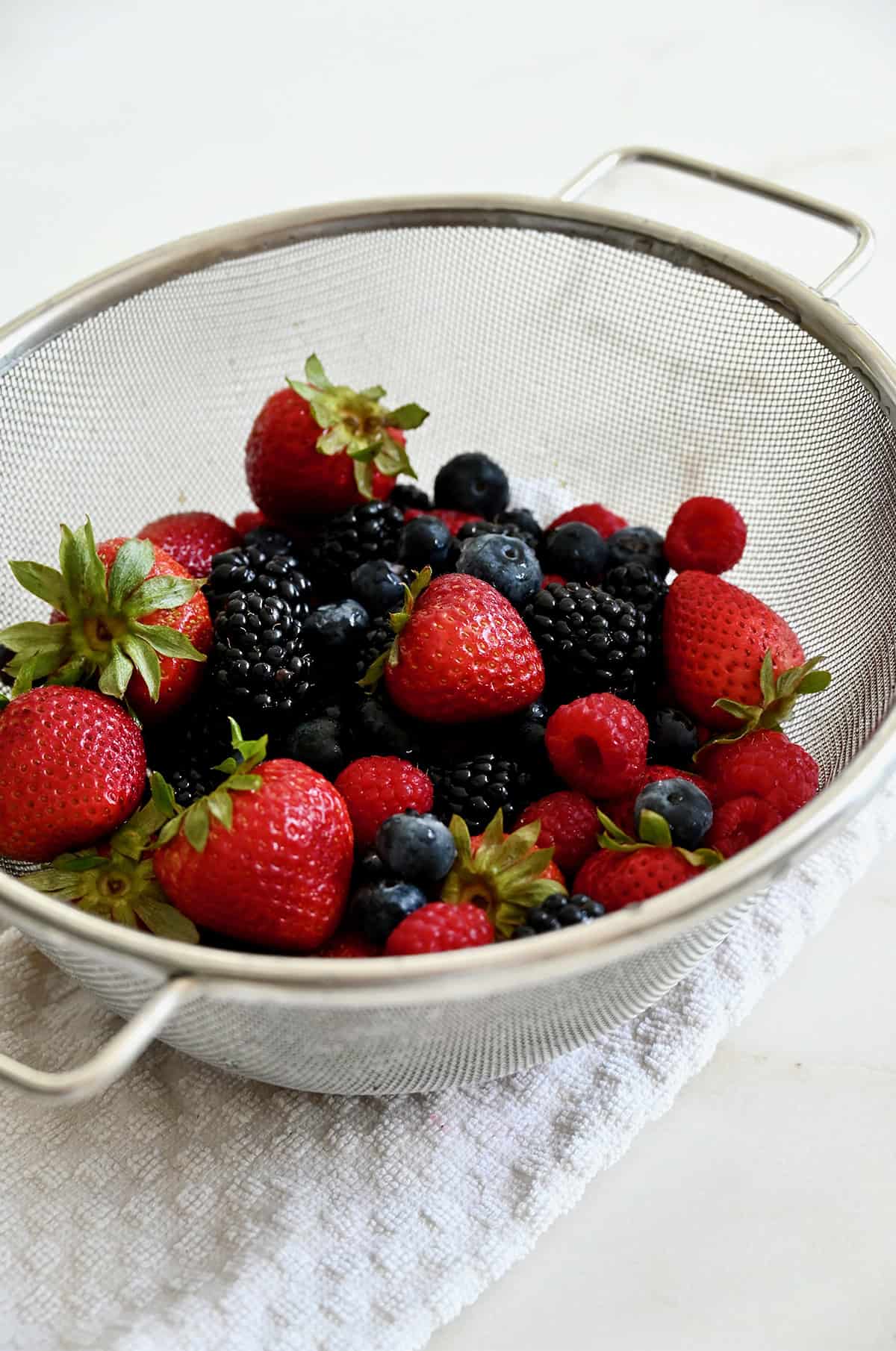 Fresh strawberries, blueberries, blackberries and raspberries in a large sieve.