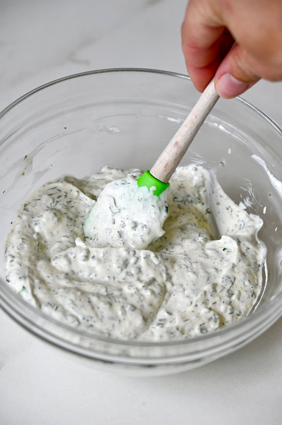 Homemade vegetable dip with fresh herbs in a mixing bowl with a rubber spatula.
