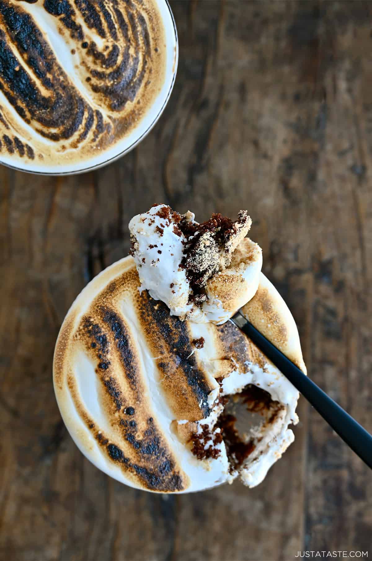A s'mores cocktail cake in a coupe glass featuring layers of moist chocolate cake, crushed graham crackers and toasted marshmallow fluff.