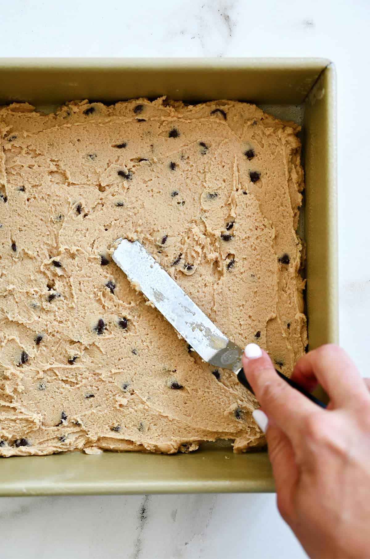 Spreading chocolate chip cookie dough in a pan with an offset spatula.