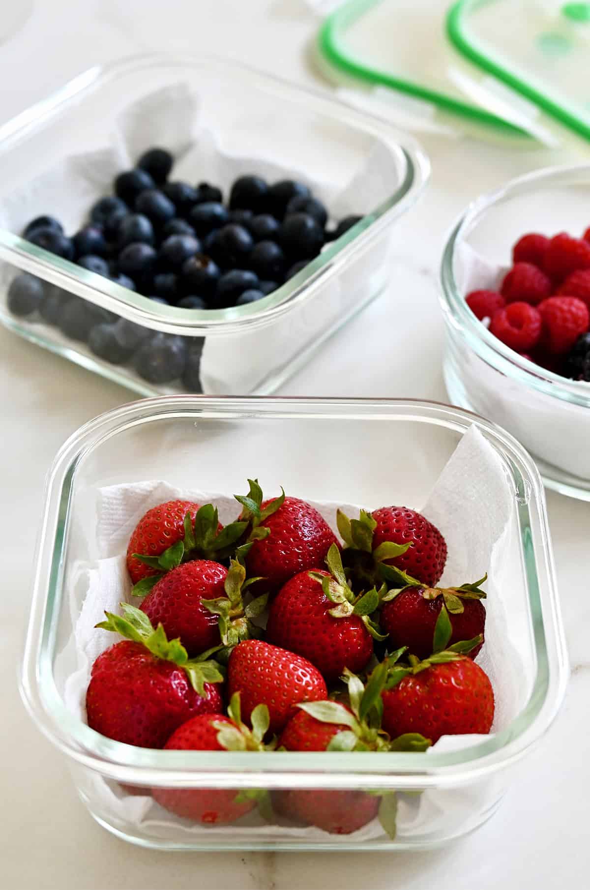 Storing fresh berries in glass containers lined with paper towels and sealed with airtight lids.