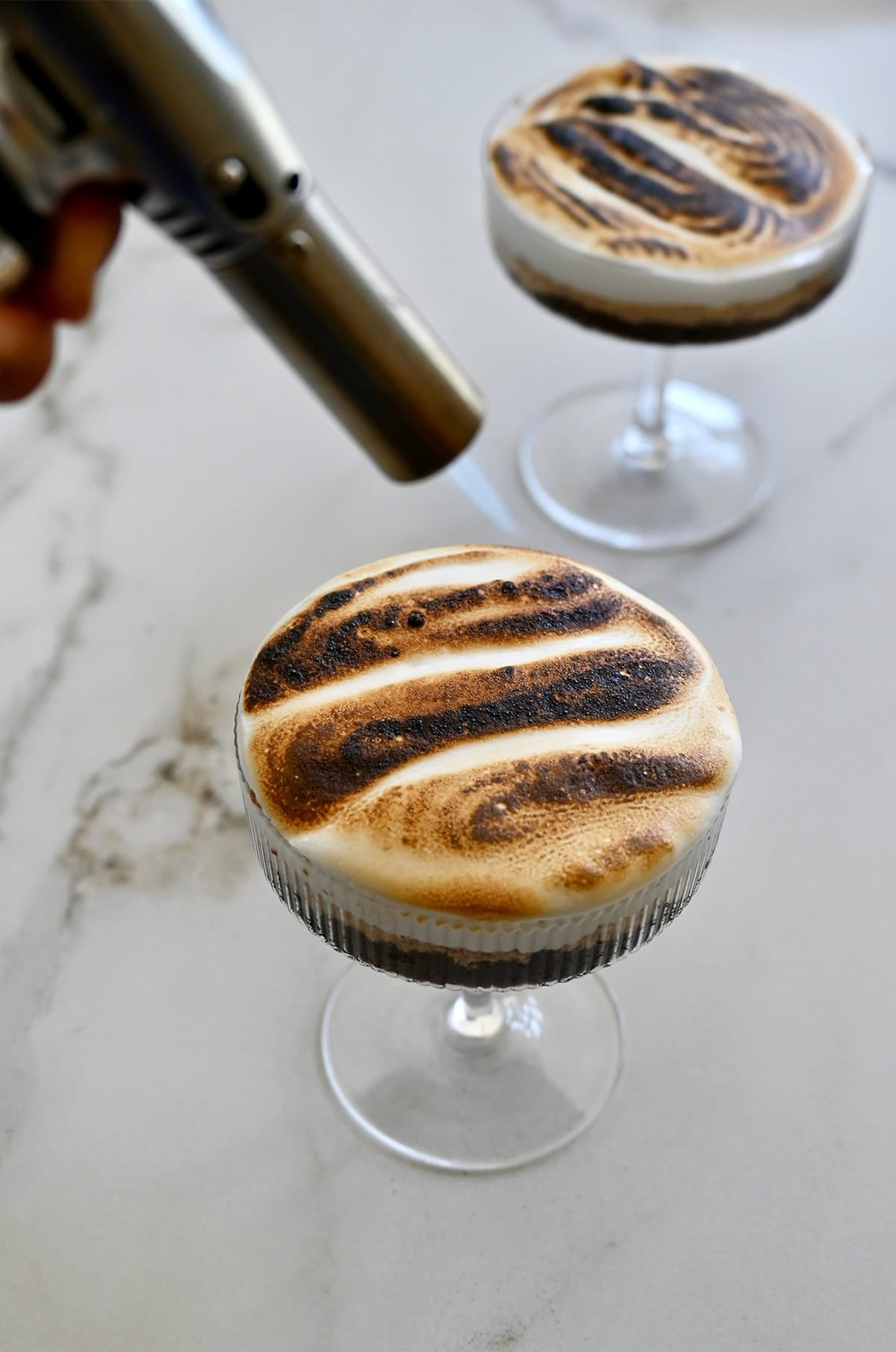 Using a kitchen torch to toast marshmallow fluff for s'mores cake.