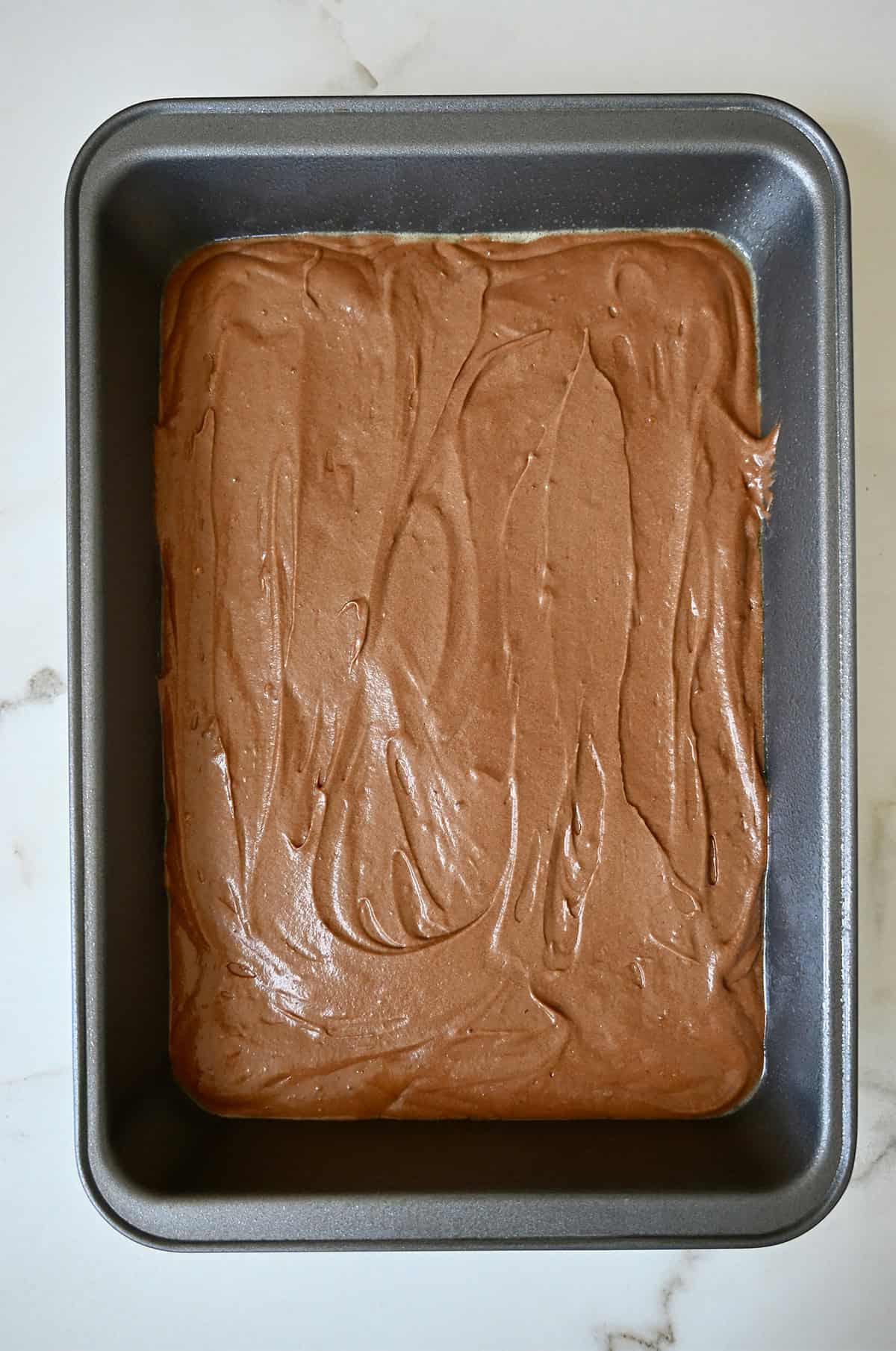 Unbaked chocolate cake in a 9x13 metal pan.