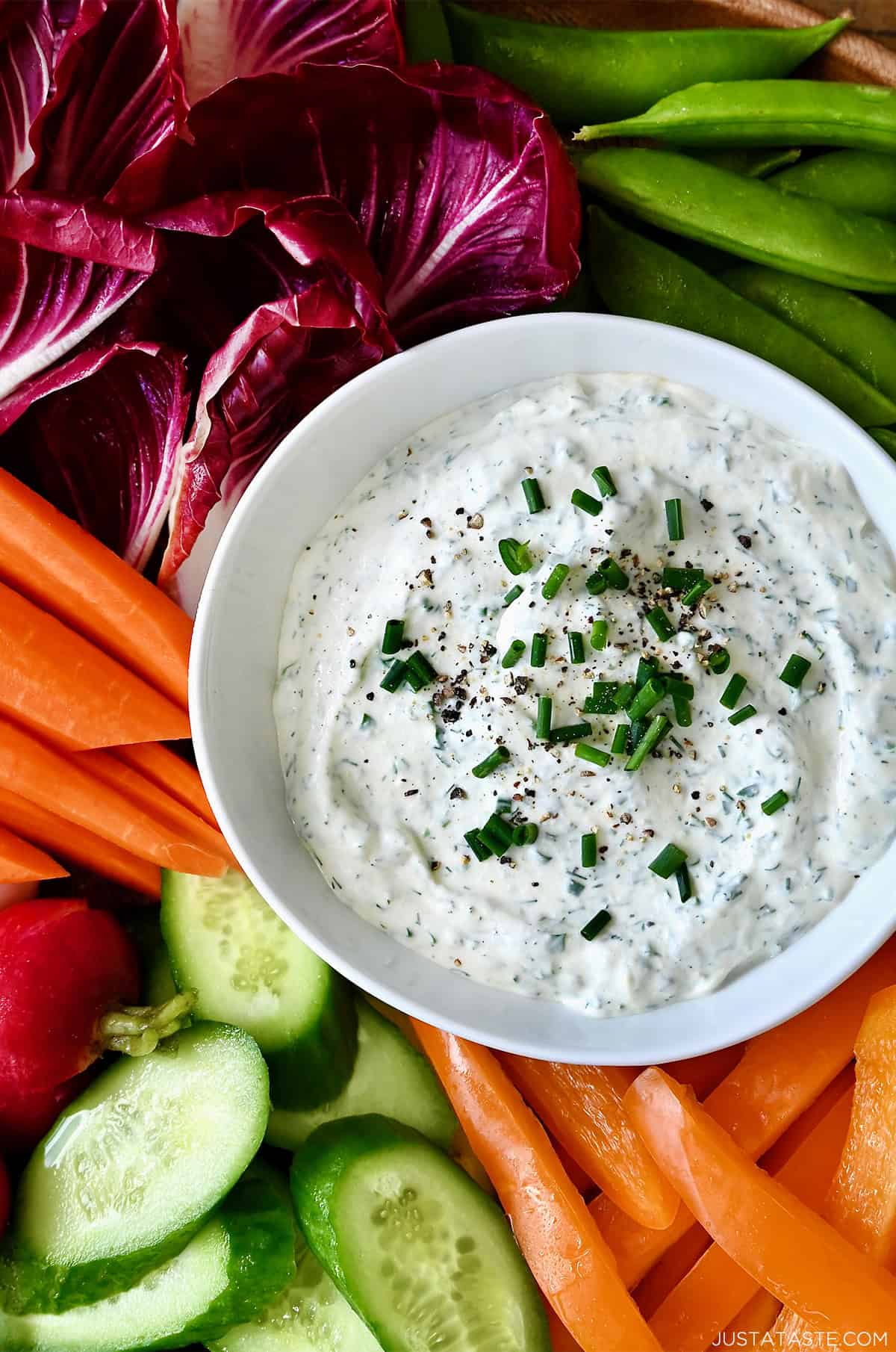 A bowl of garlic herb veggie dip on a serving platter surrounded by fresh vegetables for dipping.