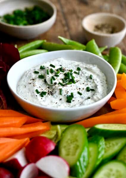 Homemade garlic herb veggie dip in a small bowl on a plate surrounded by sliced raw vegetables.