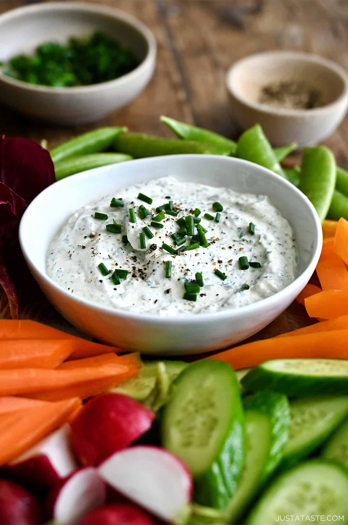 Homemade garlic herb veggie dip in a small bowl on a plate surrounded by sliced raw vegetables.