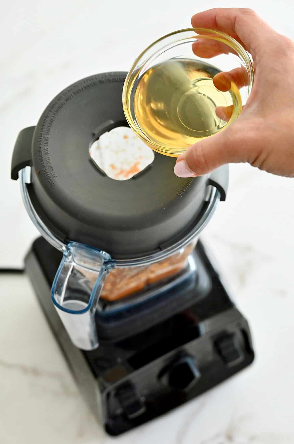 Adding avocado oil to a blender to emulsify into a creamy carrot-ginger dressing.