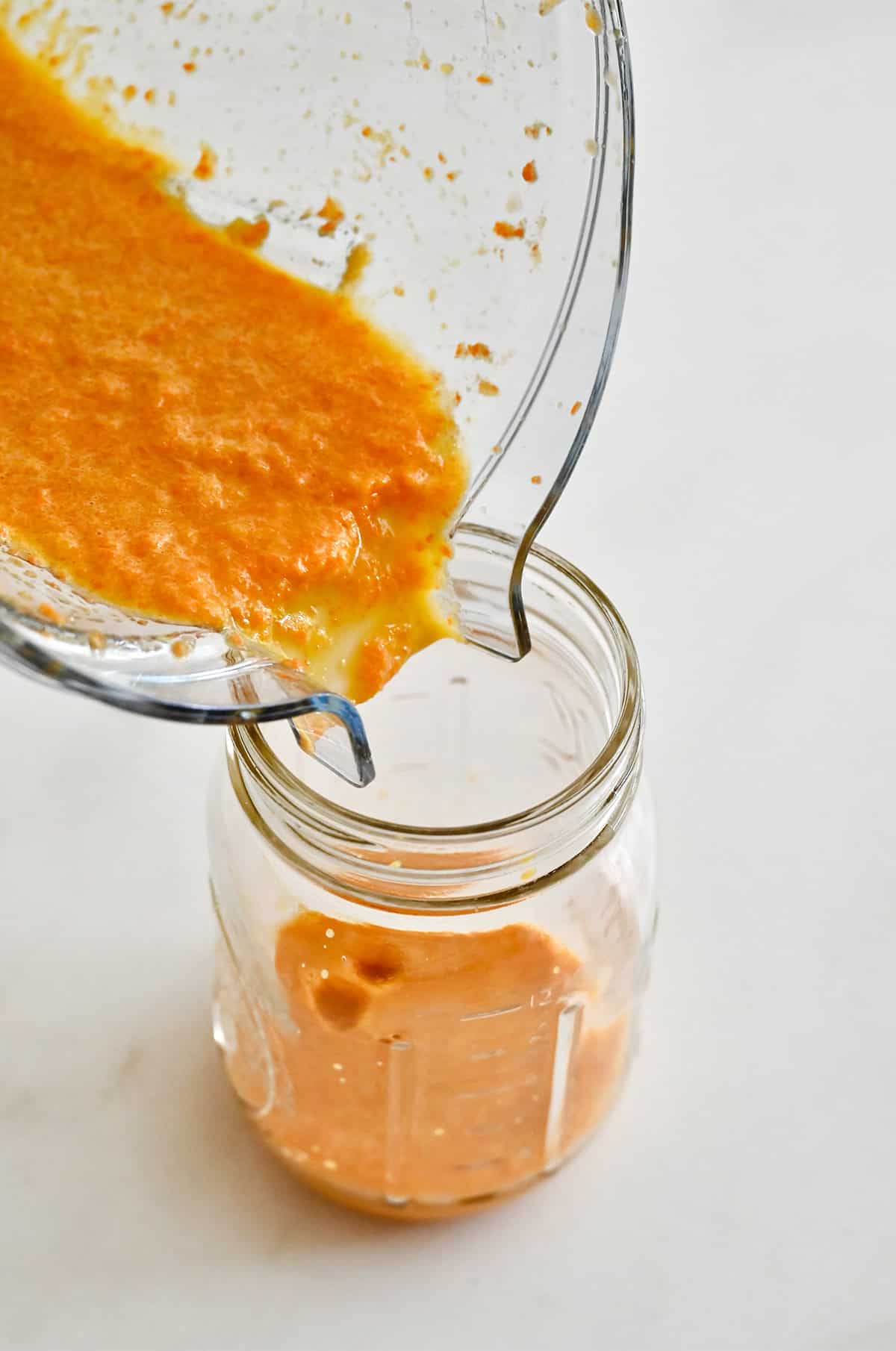 Carrot dressing is being poured from a blender into a mason jar.
