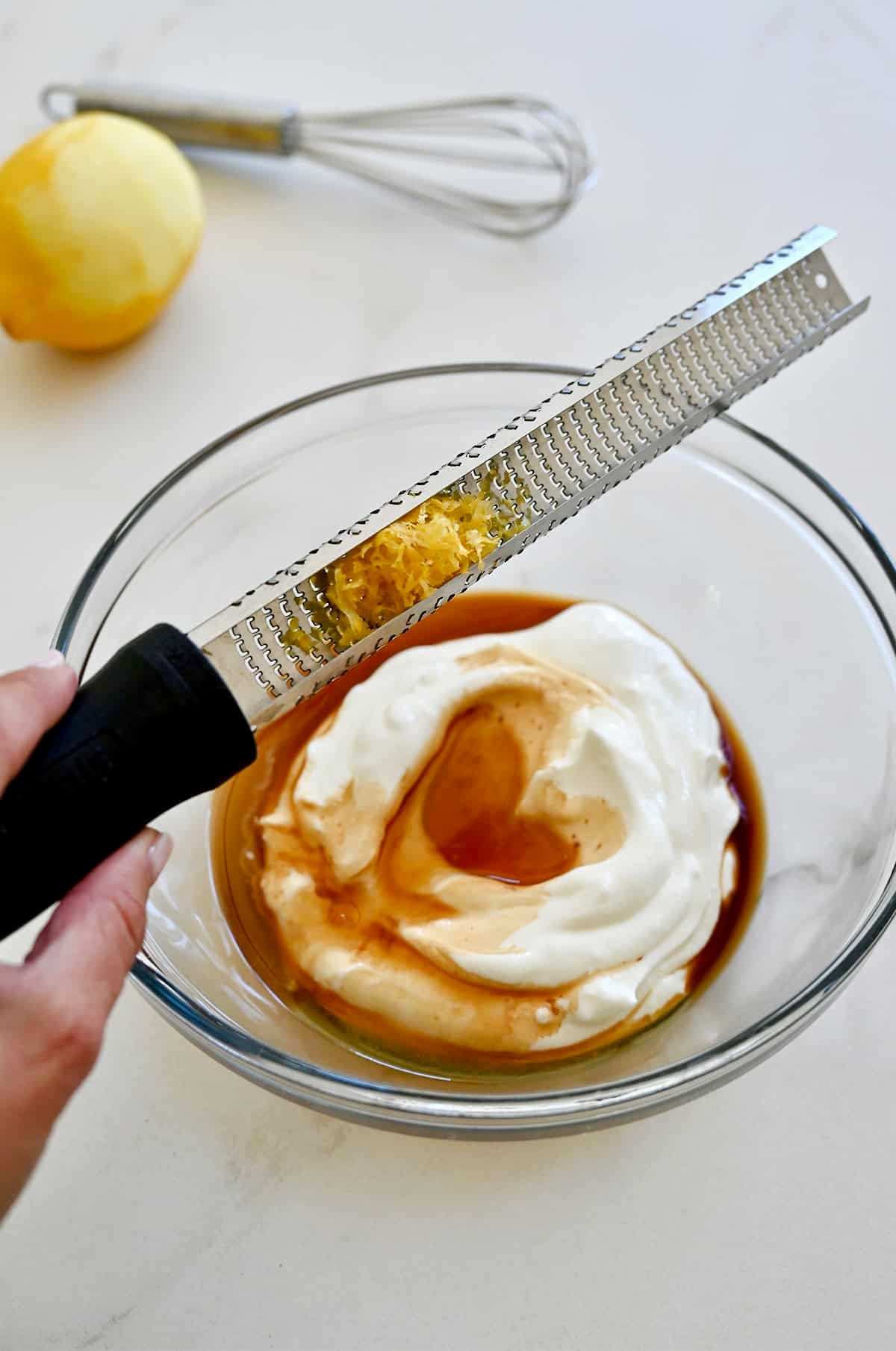 Adding lemon zest to a bowl with yogurt, honey and vanilla extract to make a fruit dip.