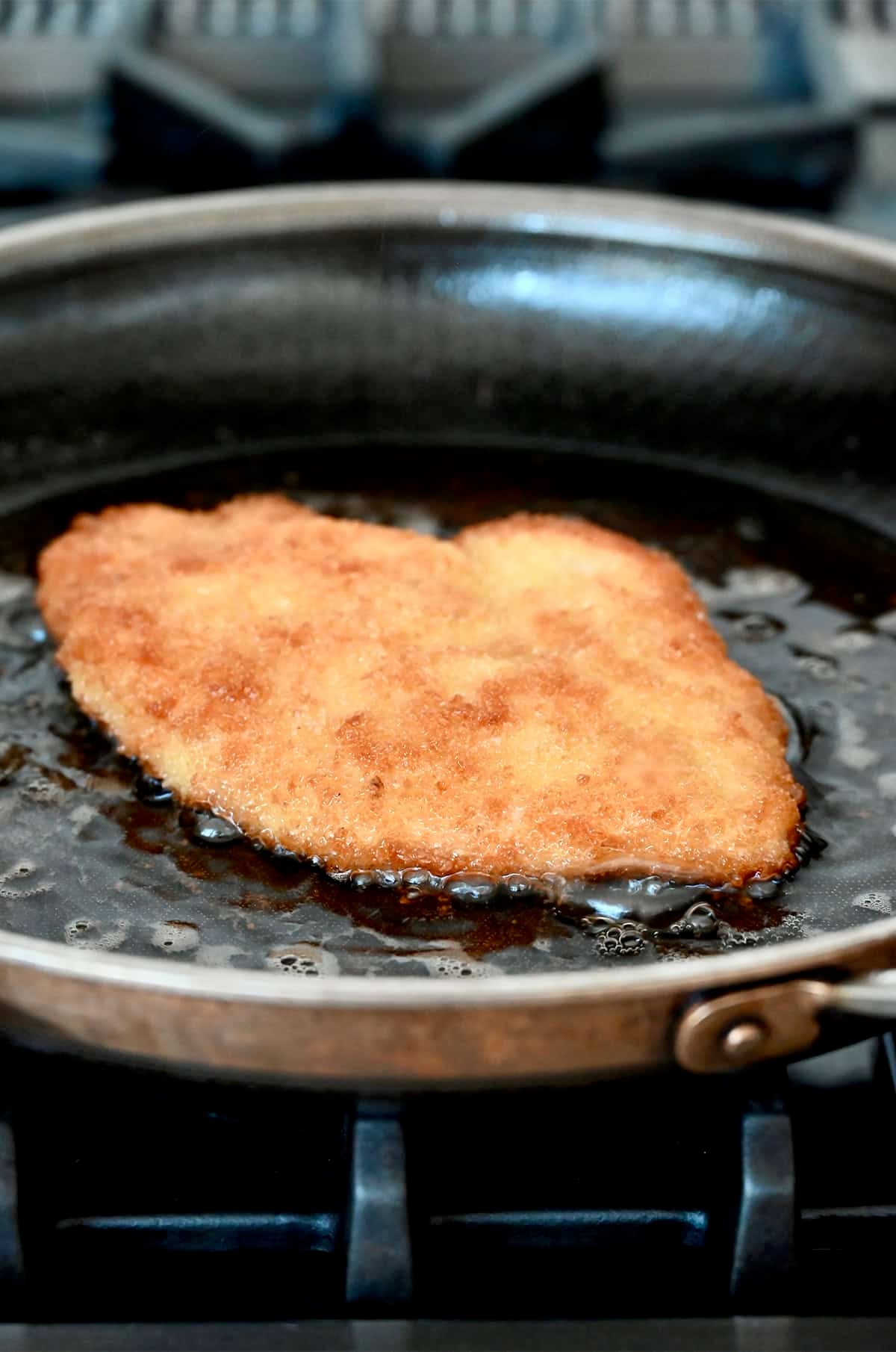 Pan-frying a breaded chicken cutlet in hot oil.